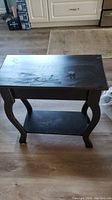 Front view of the black wooden side table showing rectangular top and curved legs.