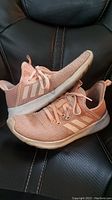Pink Adidas women's shoes showing side and top views, placed on a black leather surface.