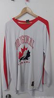 Front view of white and red long-sleeve Canada Olympic original jersey on hanger showing logo and design.