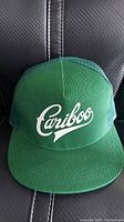 Front view of green Cariboo snapback hat with white scripted logo.
