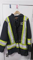 Front view of black construction jacket with yellow and silver reflective strips and 'DBC' printed on chest.