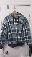 Front view of blue and white plaid zip-up sweater jacket hanging on door.