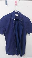 Full view of the blue Gap men's dress shirt with buttons and hanging open on white and pink hangers.