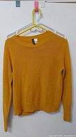 Front view of yellow mustard H&M women's sweater on hanger showing overall condition and ribbed cuffs and hem