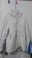 Front view of the white Helly Hansen jacket with blue stripes on sides and hood, on hanger.