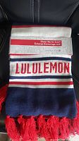Front view of Lululemon scarf showing white stripe with red LULULEMON text and red tassels.