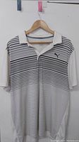 Front view of white Puma Gulf polo shirt with black and gray horizontal stripes and Puma logo on left chest.
