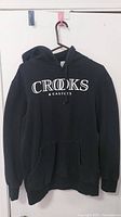 Front view of black Crooks and Castles hooded sweater with logo and front pocket.