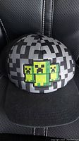 Black and grey pixelated Minecraft themed baseball hat with three Creepers on front, black bill
