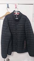 Front view of men's black quilted jacket by Tommy Hilfiger, size XXXL, hanging on wall.