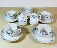 Full view of the tea set including six cups and saucers, sugar bowl with lid, and creamer, all white porcelain with blue floral motifs
