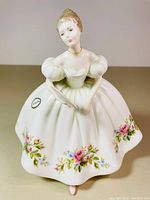 Front view of Royal Doulton bone china figurine showing white dress with floral decoration and fan in hand.