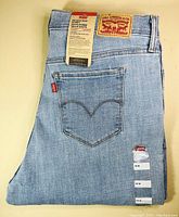 Photo shows folded light blue Levi's jeans with back pocket and Levi's red tab visible. Brown leather Levi's patch is on waistband with original Levi's tag attached.