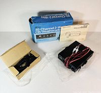 Main radio unit with wires and microphone in open small box, instruction manual, and original blue retail box in background.