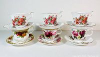 Front view of all six tea cups and saucers showing floral patterns and gold rim details