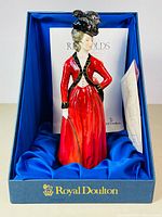 Porcelain Lady Worsley figurine seated upright in original Royal Doulton box with blue satin interior. Includes papers visible behind figurine.