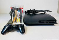 Front angle of PS3 Slim console, wireless controller, power cable, and seven game discs.
