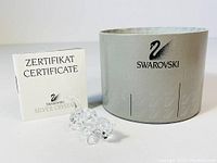 Swarovski Silver Crystal fox figurine displayed with its certificate manual and branded cylindrical box in background on white surface.
