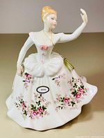 Front view showing the dancing lady in a detailed white gown with pink flower decorations and a chain tag.