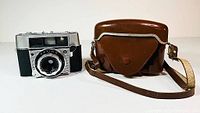 Front view of the AGFA Optima 1a camera next to brown leather carrying case with strap.