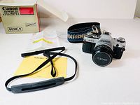 Wide shot of camera body, lens mounted, box, manual and two straps laid out