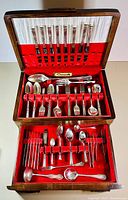 Overview of the complete open wooden chest containing the full flatware set with upper compartment for knives and lower compartment for forks, spoons, and serving pieces.