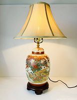 Full view of the entire lamp lit showing porcelain body, wooden base, and fabric shade