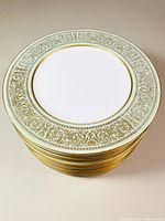 Stacked view of all 12 Mikasa dinner plates showing the pattern and gold trim around edges.