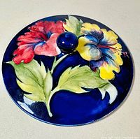 Top view of the ceramic lid showing detailed hibiscus flowers in red and yellow with green leaves on a deep blue background