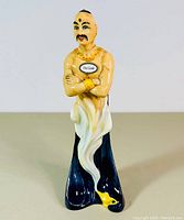 Front view of figurine showing torso, crossed arms, ‘The Genie’ label on chest, swirling lower body emerging from lamp