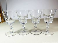 Four clear crystal Val Saint Lambert stemware glasses with faceted bases and distinct cut patterns on the bowl displayed side by side on a flat surface.