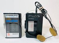 Pair of Sony Walkman cassette players side by side, one black with attached headphones and one silver with black trims