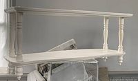 Photo of white painted antique two-shelf wall shelf made likely of pine wood, showing turned spindle supports and clean painted finish.