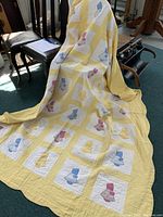 Full view of antique/vintage hand made Sunbonnet Sue quilt draped over chair showing overall pattern and size