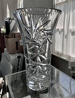 Clear tall cut glass vase with detailed cut patterns on a glass table, natural light showing the reflections and cuts.