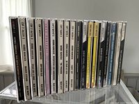 Photo of 16 jazz CDs in jewel cases lined up vertically showing titles and artists including Herbie Hancock, Barney Kessel, Wes Montgomery and more.