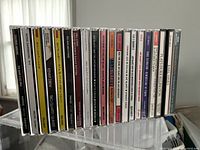 Photo of 25 jazz music CDs in their jewel cases, arranged side by side showing spine titles including Bill Evans Trio, Sergio Consuegra, Kenny Drew, Count Basie, Billie Holiday and others.