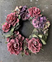 Full view of circular floral wreath with pink roses, purple flowers, and green leaves.
