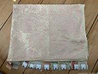 Main view of the folded silk tapestry fabric with floral pattern and attached smaller sample pieces with tags.