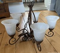 Ceiling light fixture showing five alabaster glass shades and ornate metal arms in a rust brown finish on wooden floor.