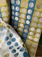 Folded vintage MCM fabric showing vertical stripes in green and blue colors with white circle motifs with line details. Partly unfolded to show pattern repeats and texture.