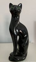 Front view of black ceramic cat-shaped vase with glossy finish showing green eyes and stylized form.