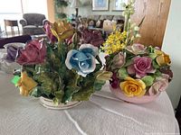 Photo showing two colorful bone china floral arrangements with detailed flowers and foliage on a table.