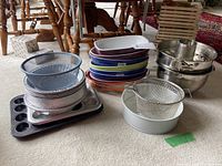 Group photo showing an assortment of ceramic and metal bakeware items including pie plates, muffin tins, mixing bowls, and strainers.