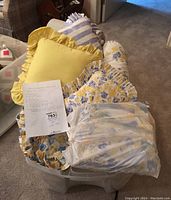 Lot contents including various floral patterned pillows, bedspread, sheets, and a bright yellow cushion with ruffles, showing overall assortment and condition.