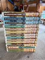 Stack of 16 hardcover books titled 'New Illustrated Encyclopedia of Gardening' with different colored spine labels.