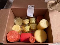 Box of assorted pillar and votive candles visible from above showing various colors and sizes including four votive candles in glass holders.