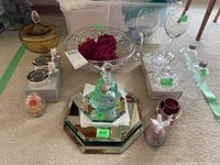 Wide view of lot contents including crystal bowl, gold candy dish, candle holders, perfume bottles, mirrored trivets, and magnifying glasses