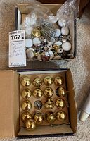 Two open boxes with various drawer pulls. The top box contains several white ceramic pulls with brass attachments and some brass pulls. The bottom box contains all polished brass drawer knobs and handles.
