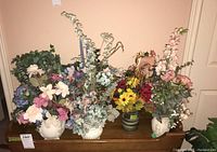 Overall view of 7 faux floral arrangements in ceramic pots placed on wooden surface against beige wall